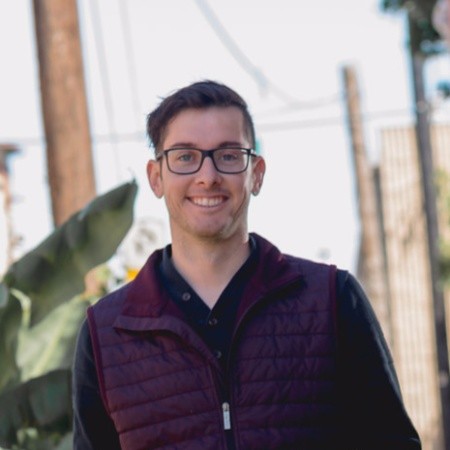 Portrait of a man with brown hair and glasses on a flat gray background.